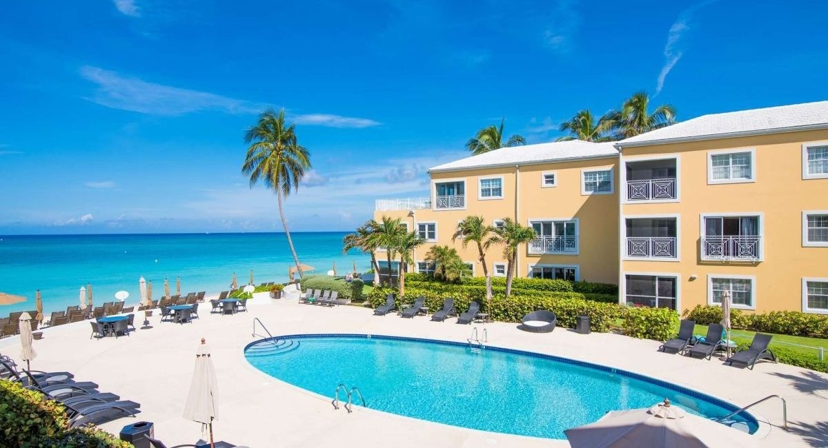 Oceanfront Vacation Rental in Grand Cayman with turquoise water in the distance and a pool with palm trees in the resort